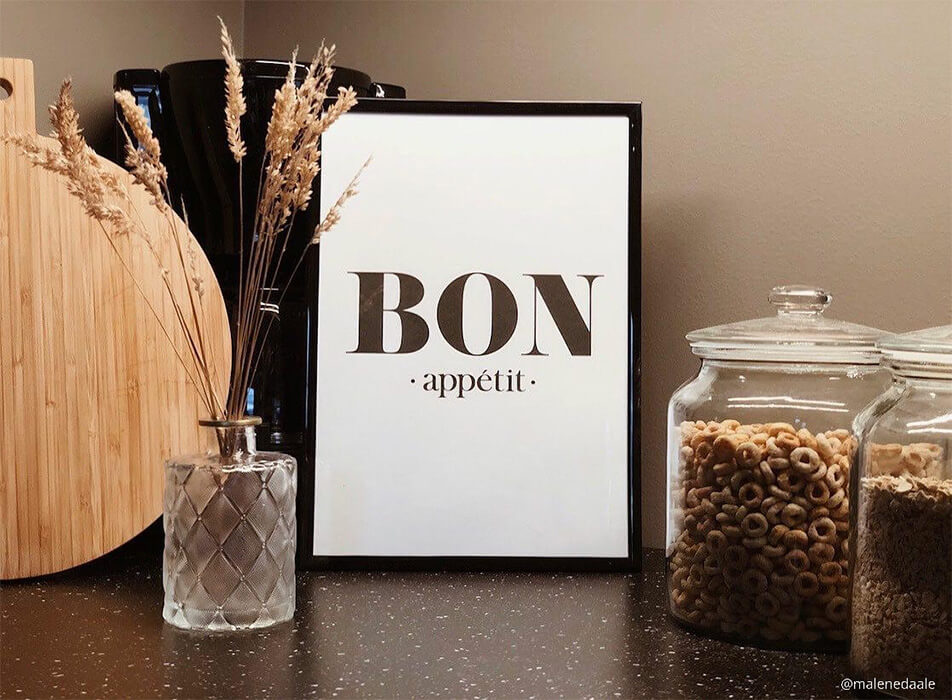Køkkenplakat med teksten Bon appétit, kaffemaskine og glasbeholdere på mørk bordplade
