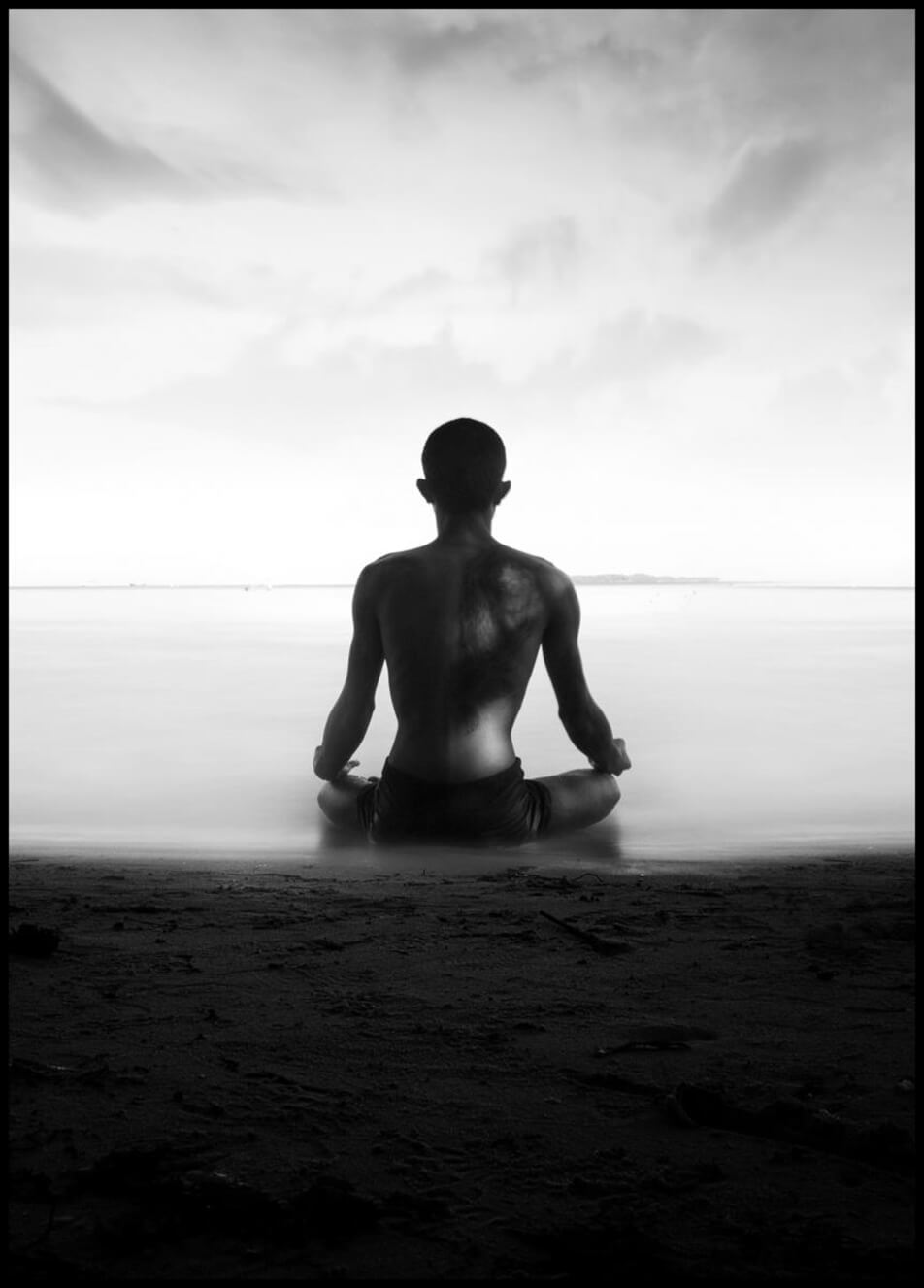 Plakat med foto, der forestiller en mand, som mediterer ved strandkant